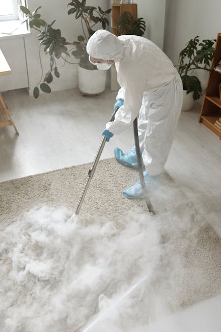 A woman using a yellow canister vacuum cleaner to deep clean a patterned beige and green area rug in a living room. She is standing on the rug, which covers polished wooden flooring, and is wearing ca